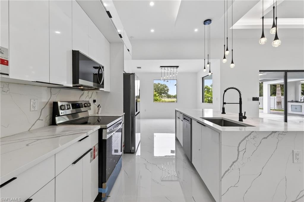Modern kitchen featuring a waterfall island with an undermount sink and matte black faucet, stainless steel appliances, white flat-panel cabinetry, and polished tile flooring