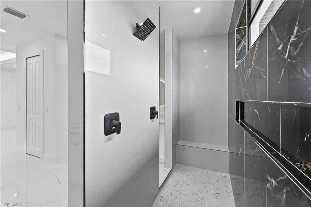 Walk-in shower featuring matte black fixtures, white tile wall, and contrasting dark marbled wall with an integrated niche