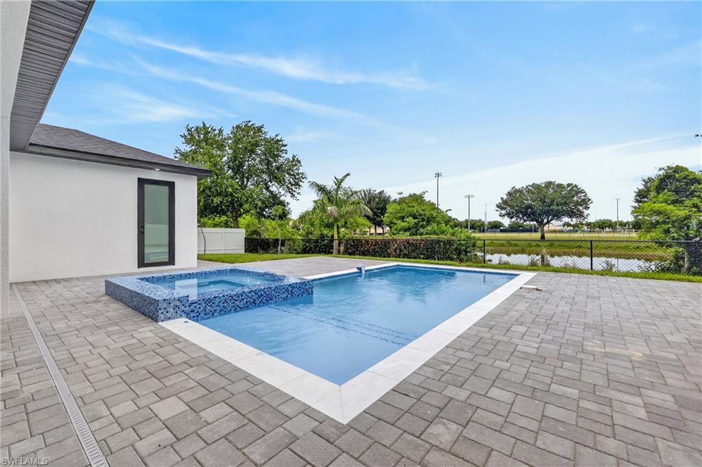 Expansive paver patio with an integrated swimming pool and elevated spa, featuring blue mosaic tile