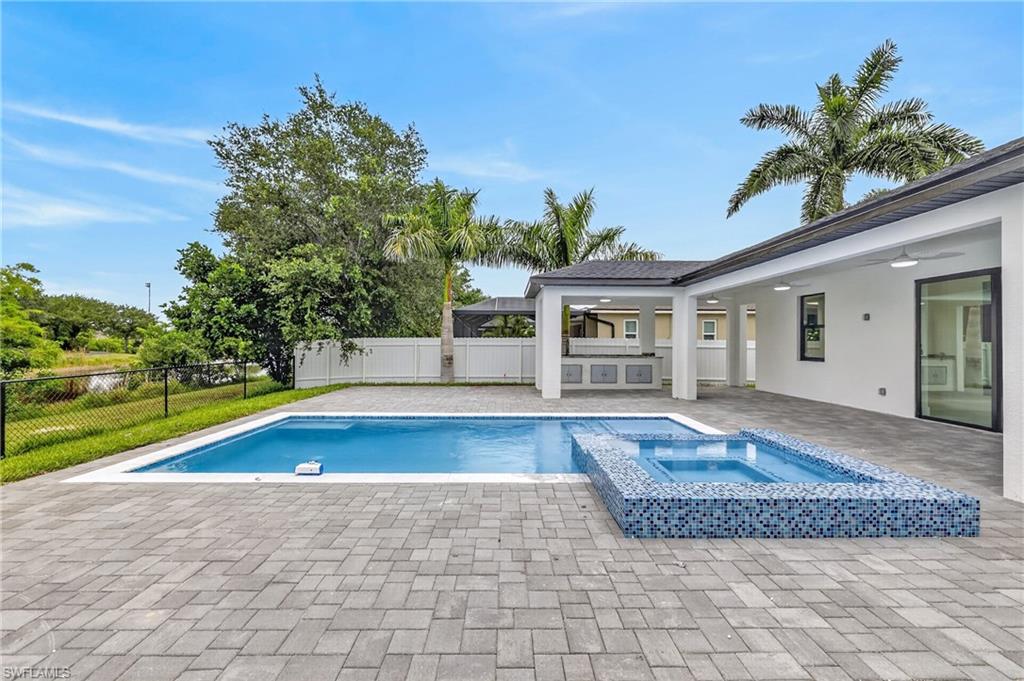 Expansive paver patio with a rectangular swimming pool, integrated spa with mosaic tile, and a covered outdoor kitchen featuring built-in cabinetry and a sink