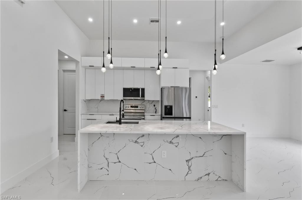 Modern kitchen featuring a waterfall island with veined quartz countertops, white cabinetry, stainless steel appliances, and sleek pendant lighting
