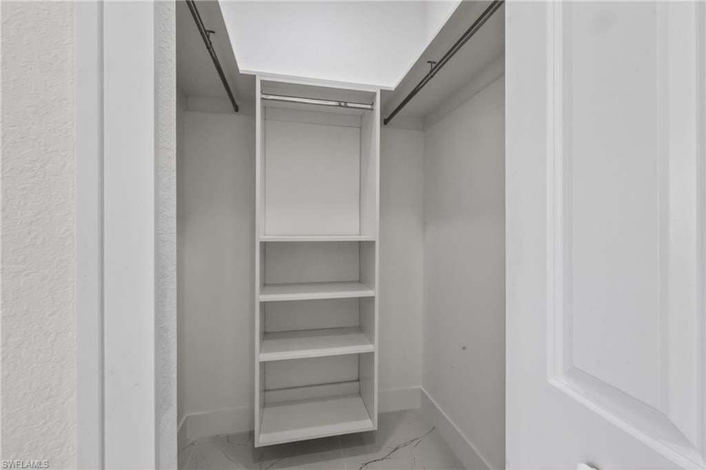 Closet organization system featuring built-in shelving, hanging rods, white paneling, and a white baseboard
