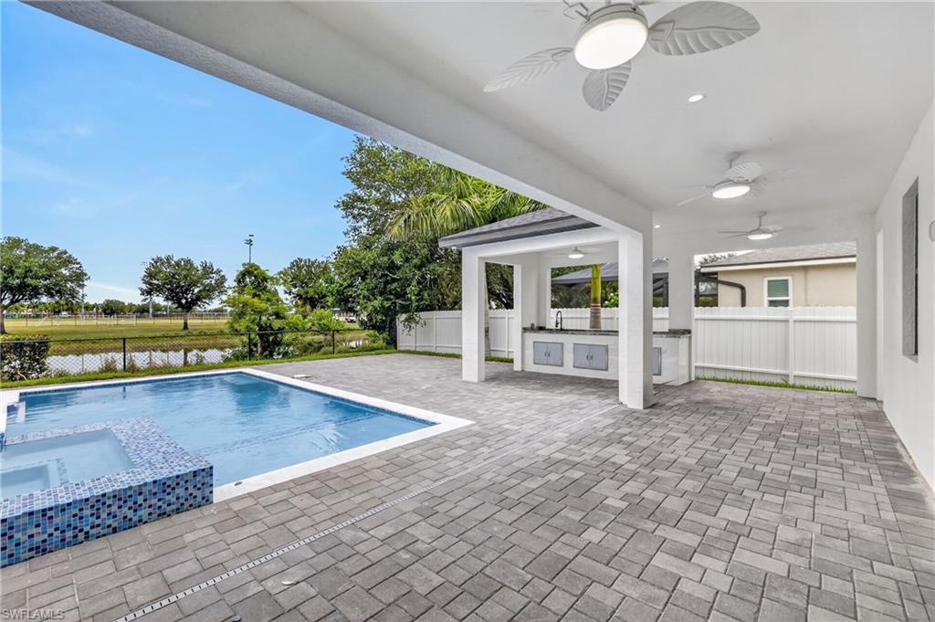 Expansive outdoor living area featuring a rectangular pool with an integrated spa, a built-in outdoor kitchen with a sink and cabinetry, a covered patio with ceiling fans and recessed lighting, and paver flooring