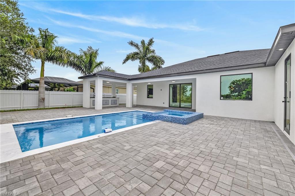 Expansive paver patio with a rectangular swimming pool, integrated spa, and covered outdoor kitchen
