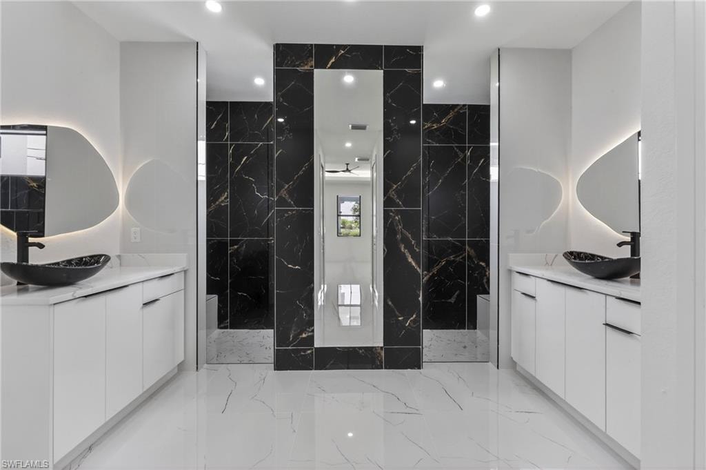 Dual vanities featuring white cabinetry and countertops, vessel sinks, and backlit mirrors