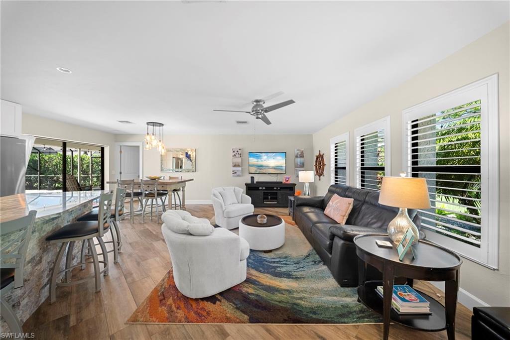Open-concept living space featuring wood-finish flooring, a contemporary ceiling fan, and multiple windows with plantation shutters