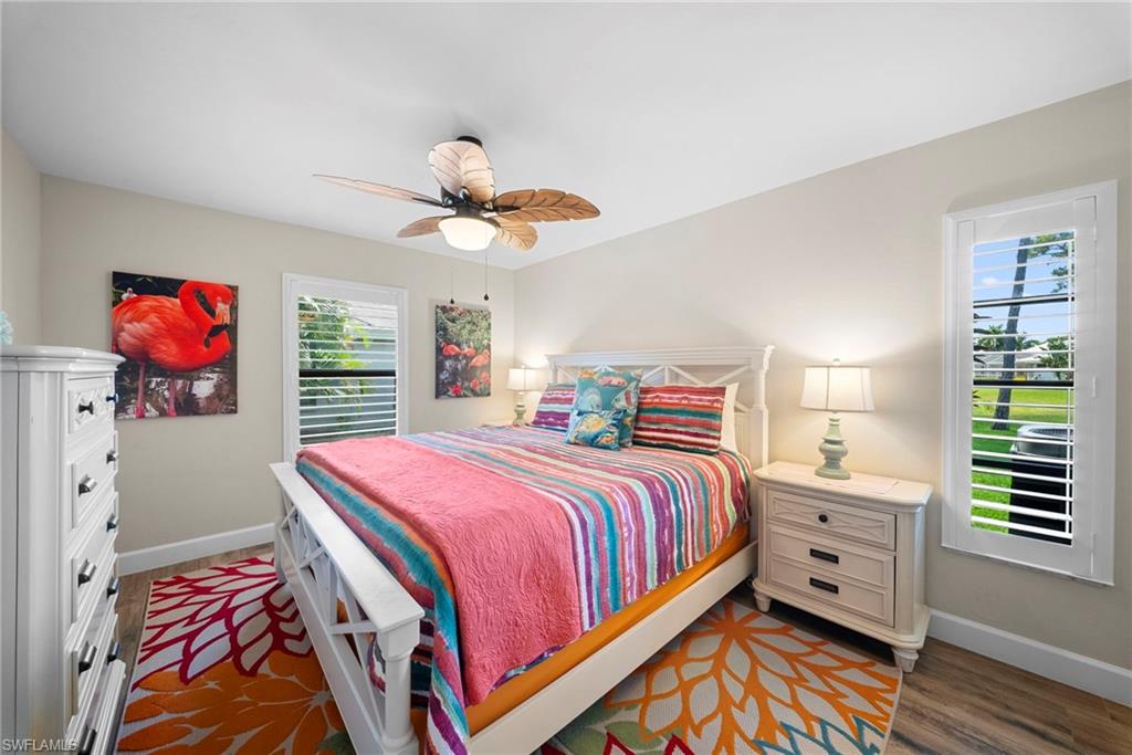 Spacious bedroom featuring wood-finish flooring, a ceiling fan with light fixture, and two windows with plantation shutters