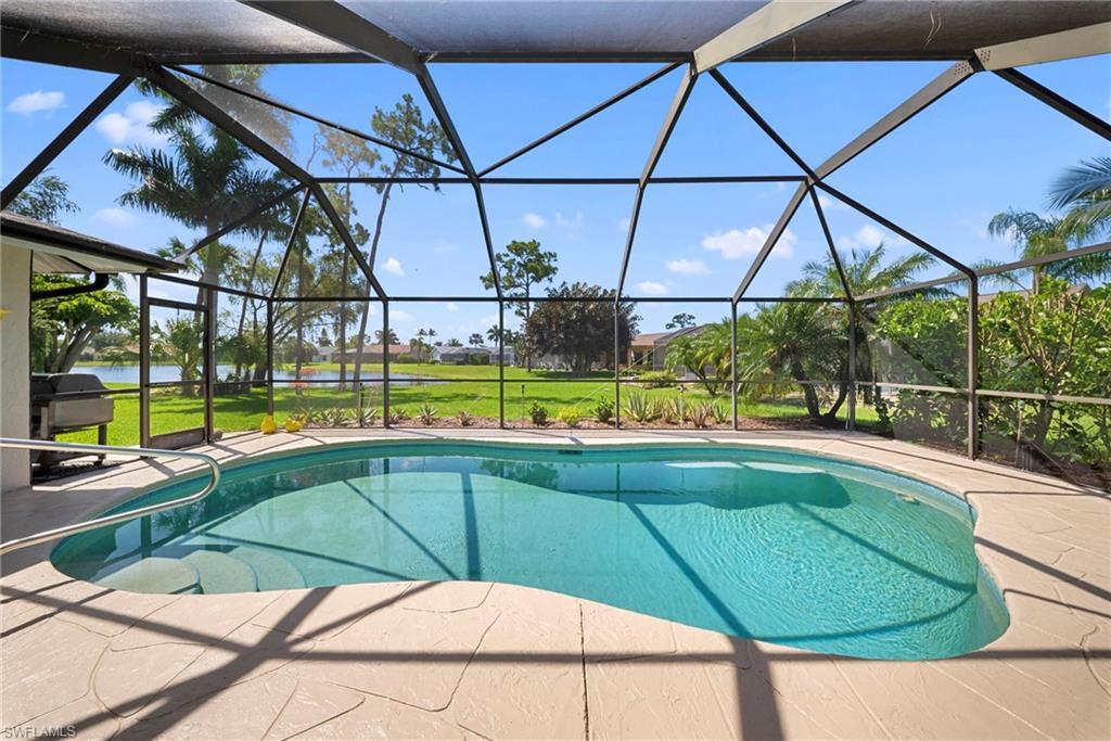 Screened lanai featuring a freeform pool with steps, a surrounding patio with textured light-colored pavers, and mature tropical landscaping
