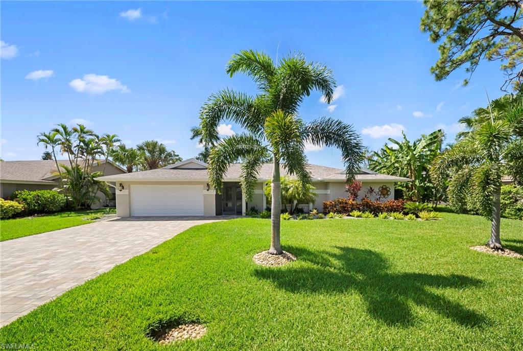 Exterior featuring a paved driveway, a two-car garage, and a lush front lawn
