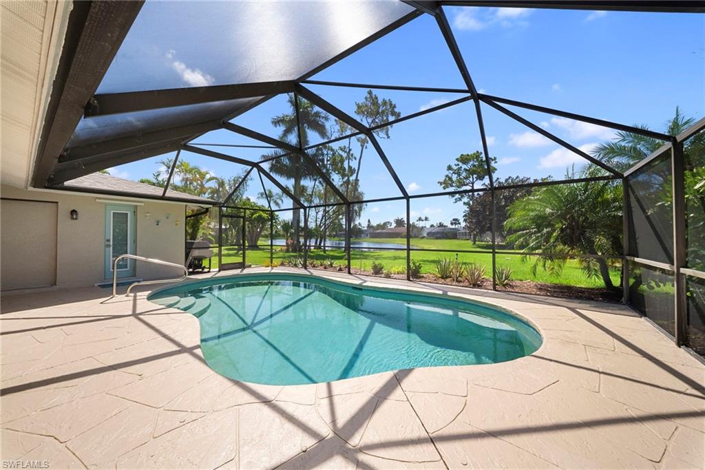 Screened enclosure with a freeform swimming pool, spacious paver patio, and lush green landscaping