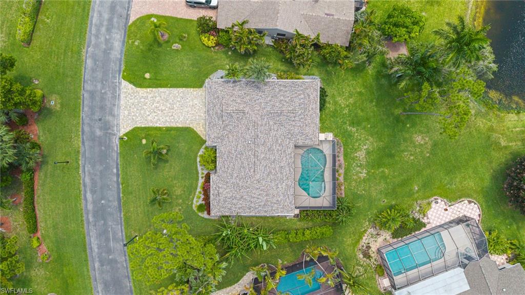 Aerial perspective showcasing a property with a distinct paved driveway, an inground swimming pool with a screen enclosure, and a shingle roof