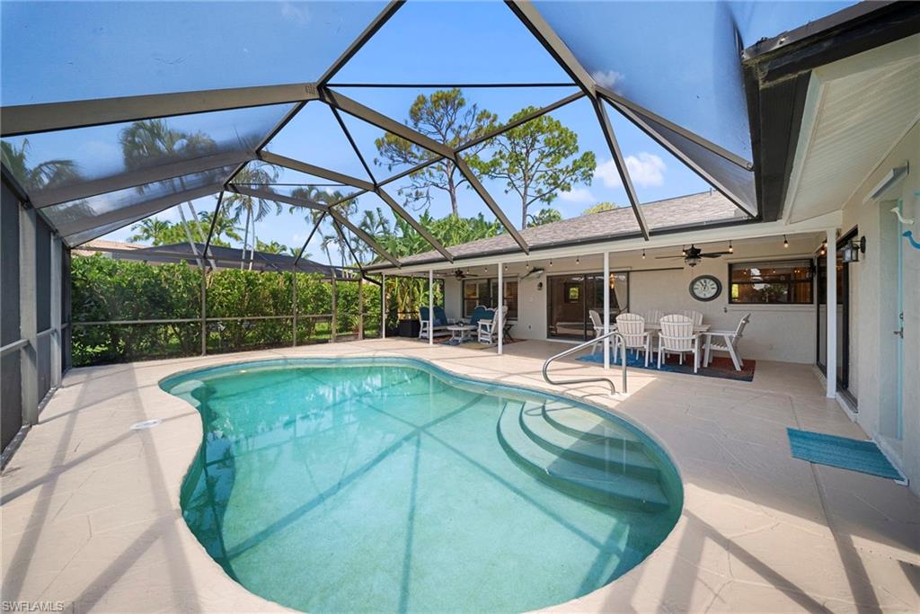 Screened-in freeform pool with integrated steps, surrounded by a light-colored paved deck