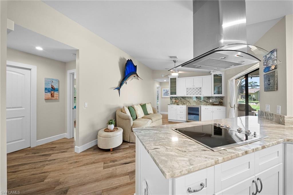 Kitchen island featuring a built-in cooktop, light-toned stone countertops, and white cabinetry with chrome hardware