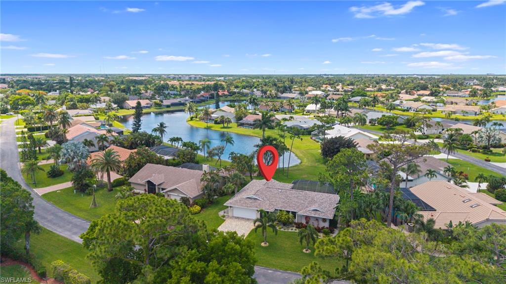 Lakeside property featuring a spacious lot, mature palm trees, an attached garage, and a tiled roof, set within a residential community with water access