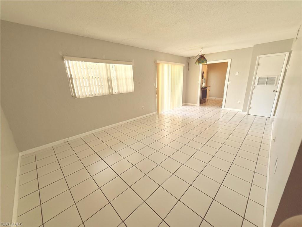 Spacious interior room featuring light-colored tile flooring, neutral wall tones, a large window with vertical blinds, and a sliding glass door