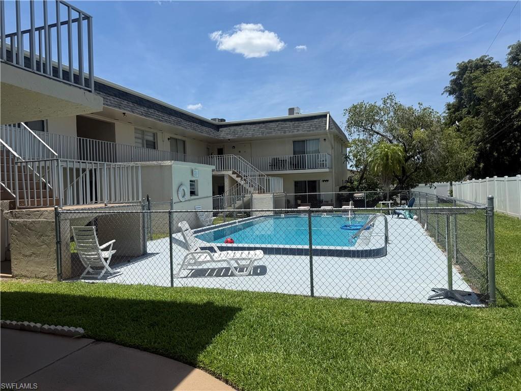 Outdoor swimming pool surrounded by a chain-link fence, concrete decking, and lush green lawn