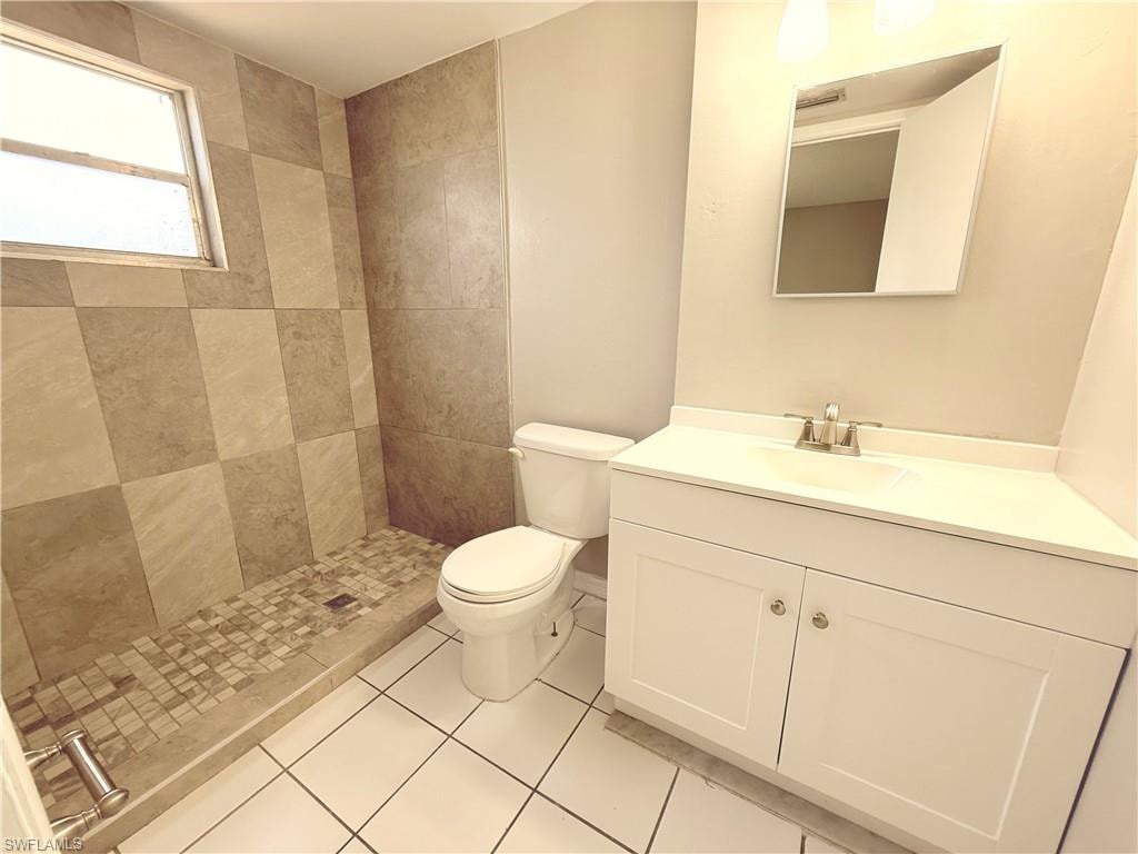 Bathroom with tiled shower enclosure, white square floor tiles, and a white vanity with an integrated sink