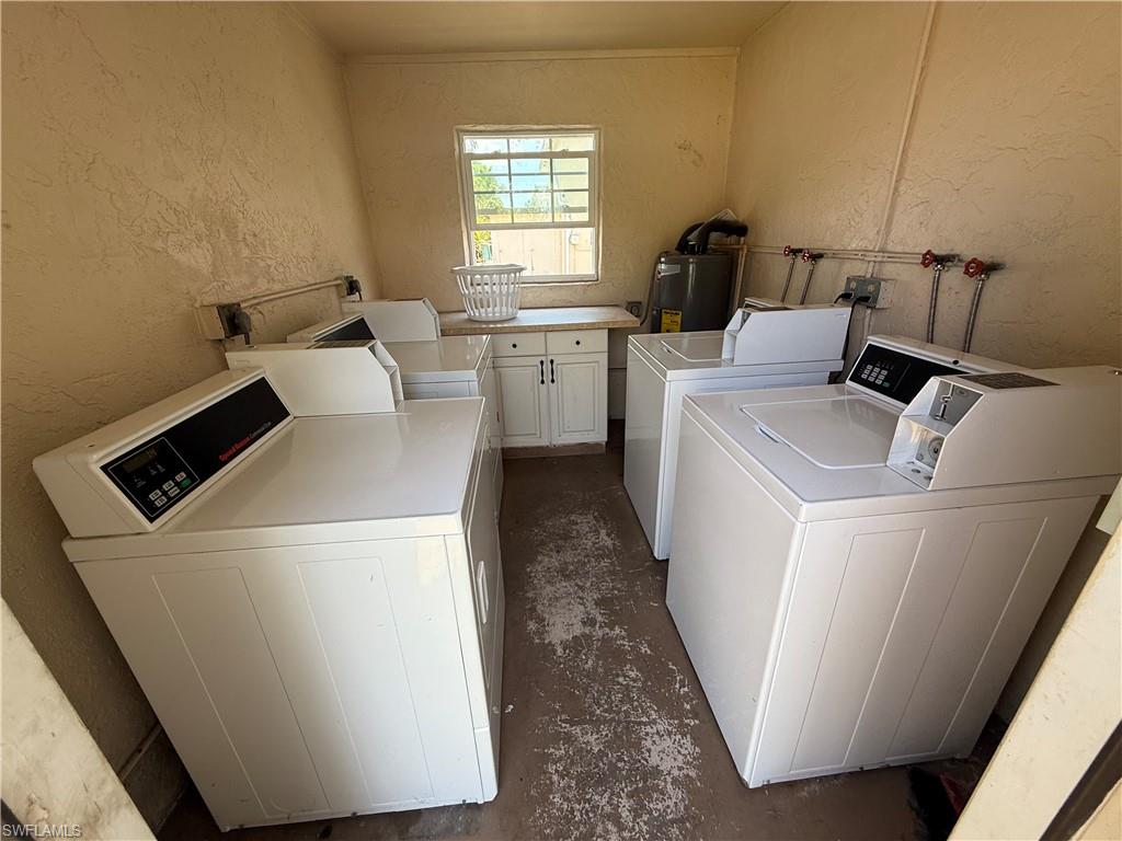 Dedicated laundry area featuring multiple top-loading machines, built-in cabinetry with a light-toned countertop, and a window providing natural light