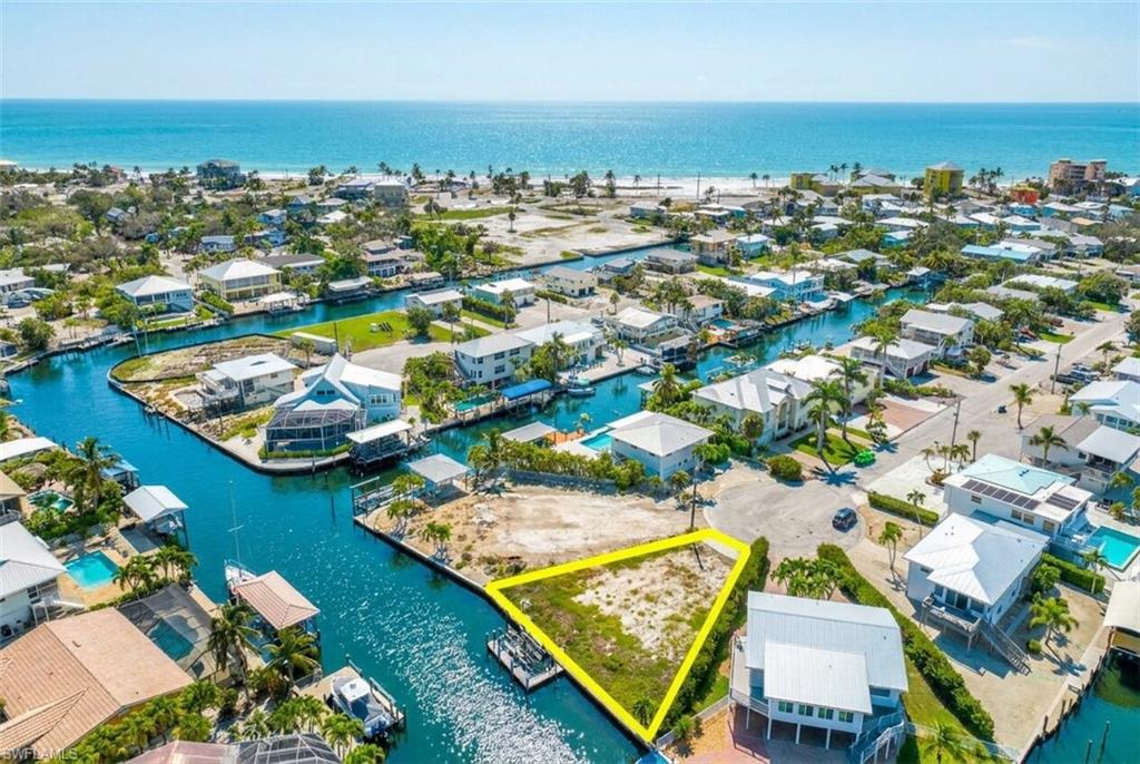 Vacant canal-front lot featuring direct Gulf access and a sandy beach shoreline in the background - Virtually Edited Image