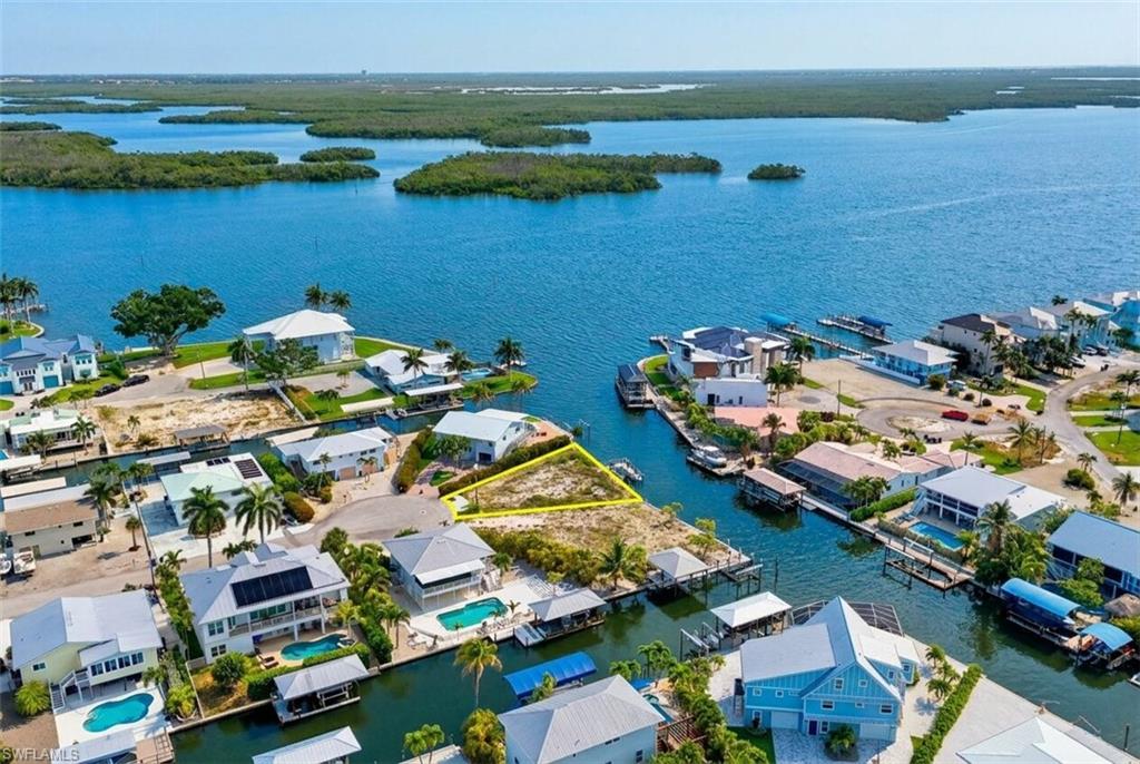 Waterfront property featuring direct canal access, an undeveloped lot, and surrounding residential structures - Virtually Edited Image