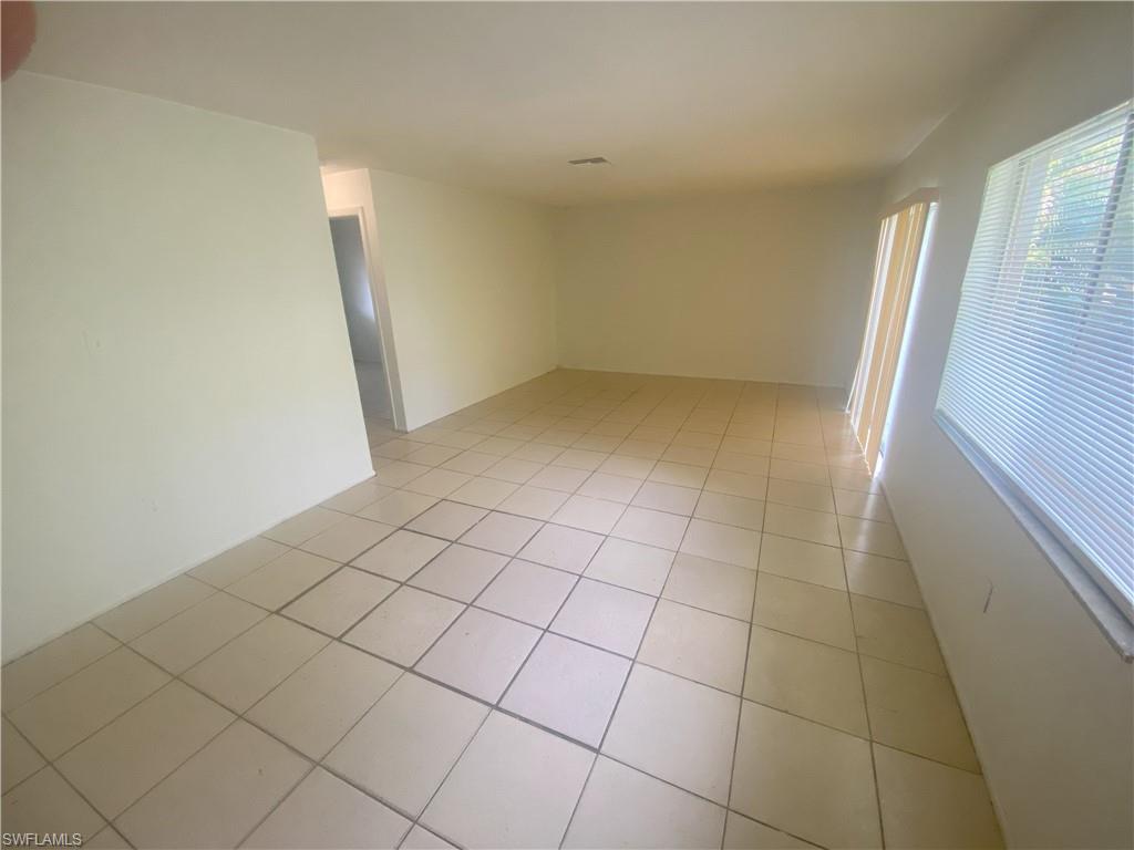 Expansive room featuring light-toned tile flooring, neutral wall finishes, and multiple windows with horizontal blinds