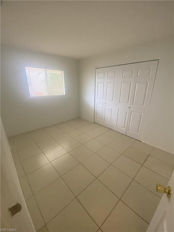 Room featuring neutral-toned floor tiling, a single window with horizontal blinds, and a built-in closet with bi-fold doors
