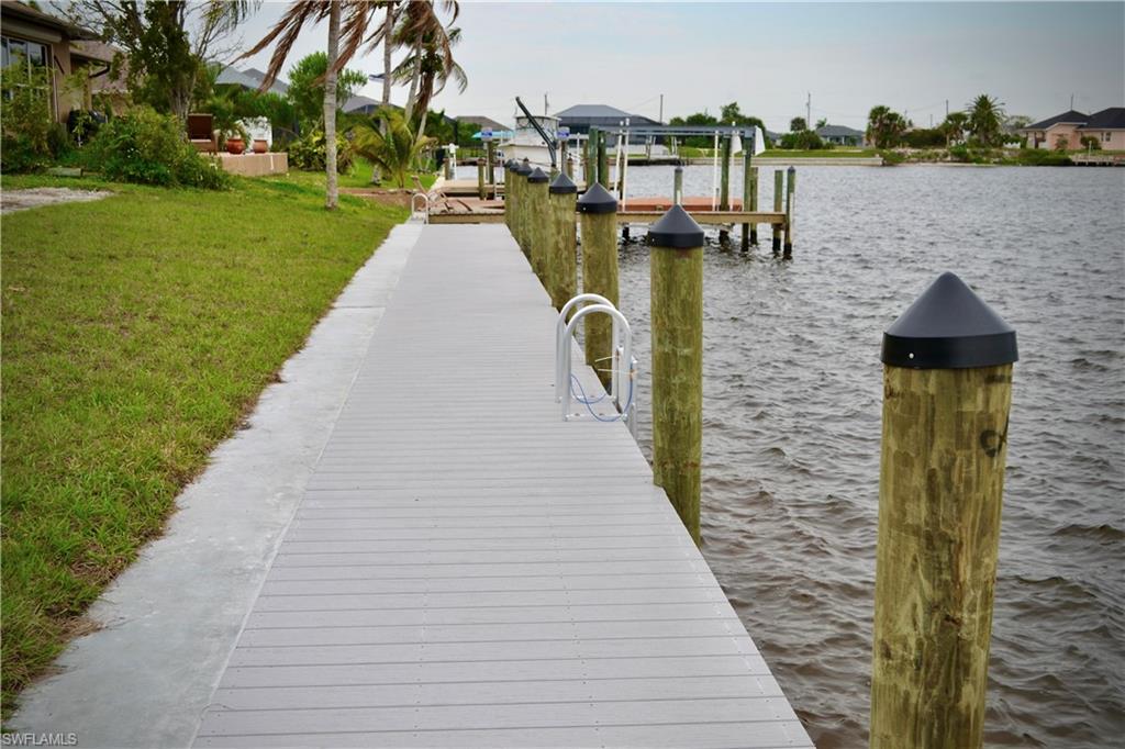 View of dock with a lawn and a water view