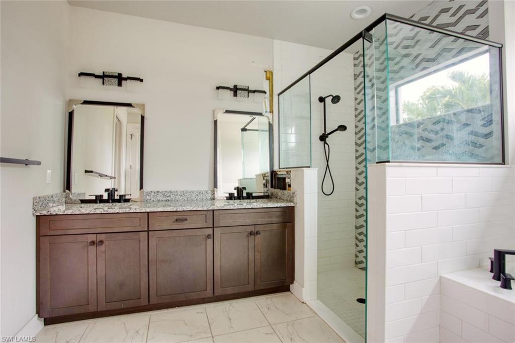 Bathroom featuring a dual vanity with granite-finish countertops, dark wood-finish cabinetry, and framed mirrors