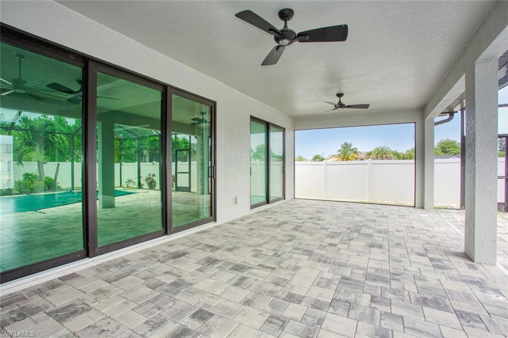 Expansive covered patio featuring patterned paver flooring, multiple ceiling fans, and a white privacy fence
