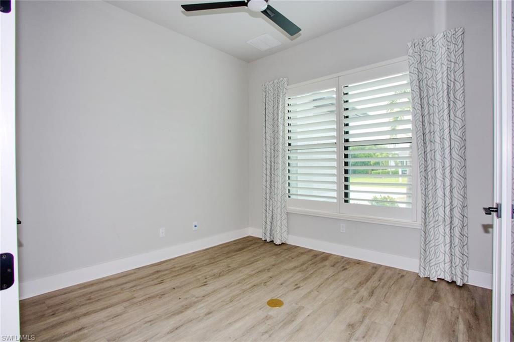 Room featuring wood-finish flooring, a ceiling fan with integrated lighting, and a large window with plantation shutters