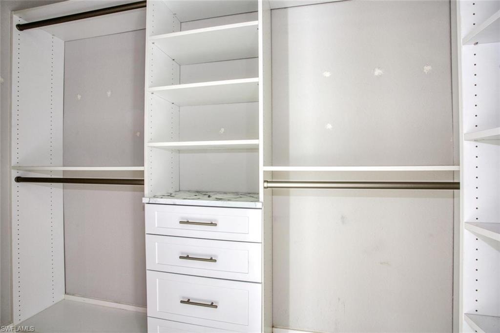 Built-in closet system featuring white shelving, multiple hanging rods, three drawers with bronze hardware, and a stone-finish countertop