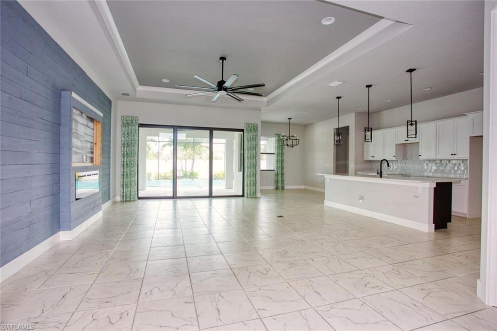 Spacious open-concept living area featuring large format tile flooring, a tray ceiling with a ceiling fan, a shiplap accent wall with a built-in media niche, and sliding glass doors opening to the exterior