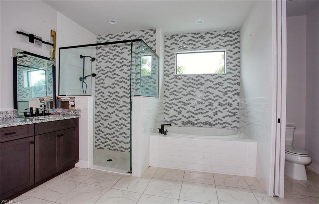Contemporary bathroom featuring a walk-in shower with black-framed glass enclosure, an integrated soaking tub, a dual vanity with a granite countertop, patterned tile accents, and large format floor tiling