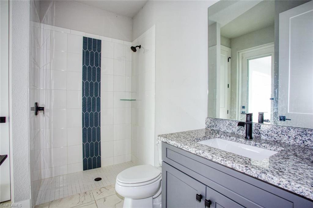 Bathroom featuring a walk-in shower with white subway tile and a dark blue picket tile accent, black shower fixtures, a white toilet, and a vanity with a light gray cabinet, a granite countertop, and a rectangular undermount sink with a black faucet