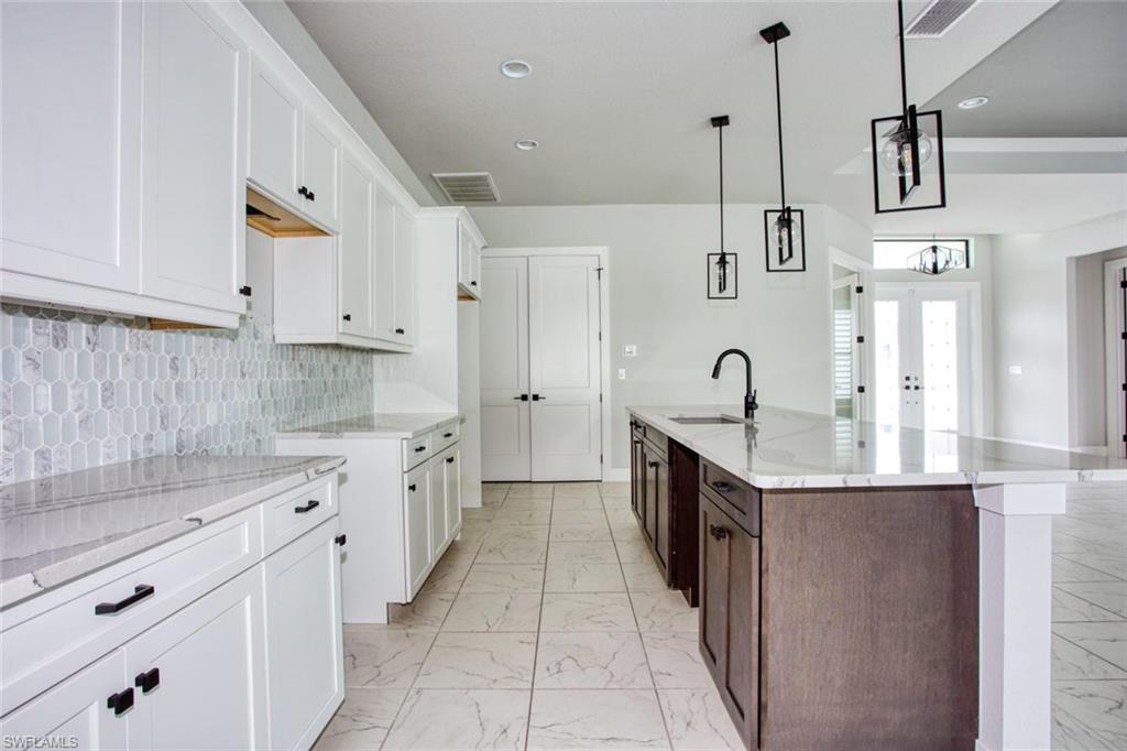 Spacious kitchen featuring an expansive center island, white shaker cabinetry, light-toned countertops, a mosaic tile backsplash, and large format tile flooring