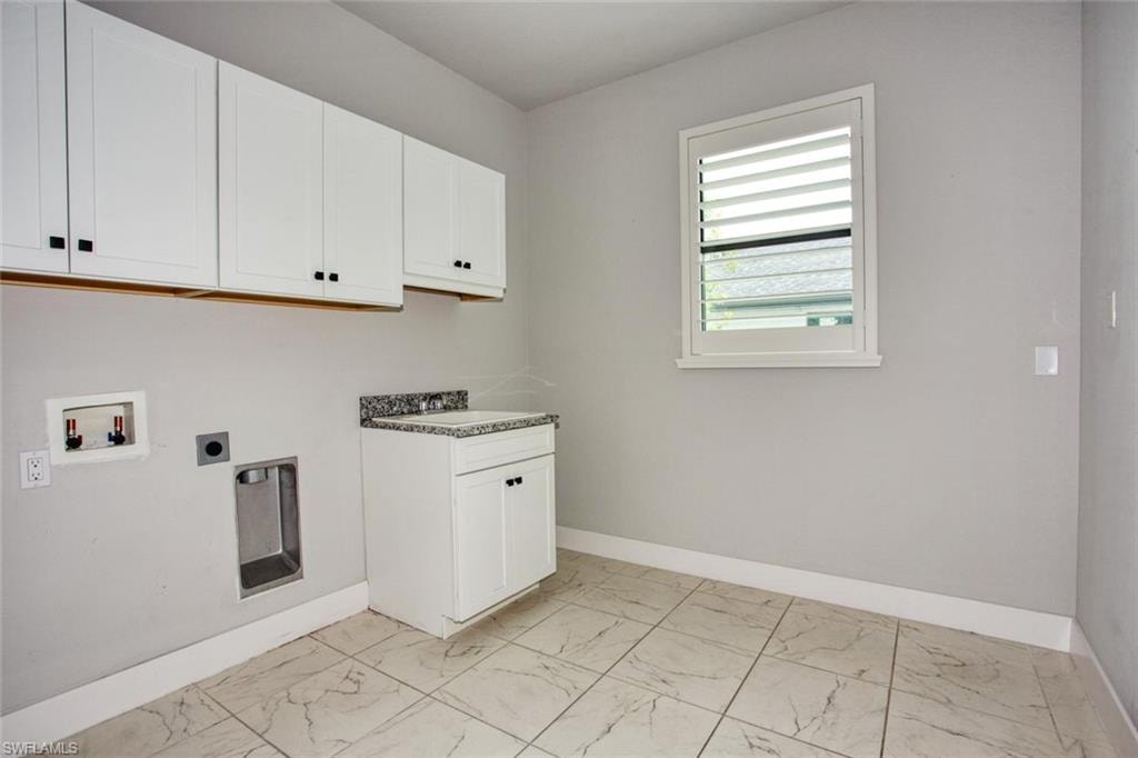 Utility space featuring overhead white cabinetry, a white base cabinet with a speckled countertop, a louvered window, and light-toned tile flooring