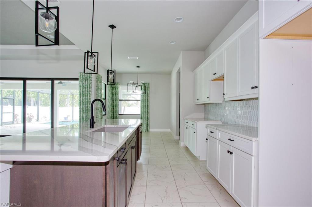 Open-concept kitchen featuring a large island with an undermount sink and matte black faucet, white shaker cabinetry with dark hardware, a light-toned tile backsplash, and recessed lighting