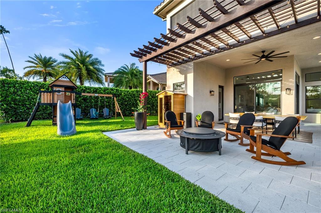 Spacious outdoor patio area featuring a wooden pergola, playground, sauna and fireplace