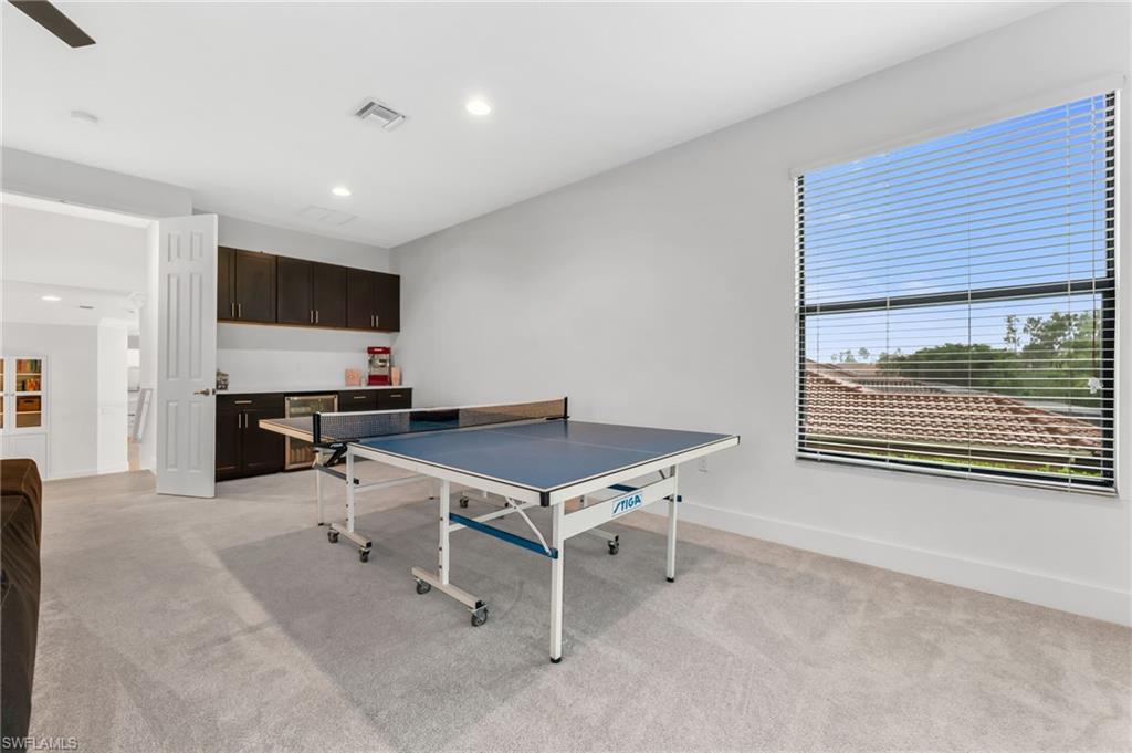 Spacious bonus room featuring plush carpet flooring, a built-in wet bar with dark cabinetry, recessed lighting, and a window