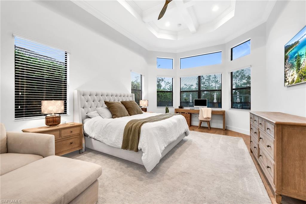 Spacious room featuring a tray ceiling with a fan, a bay window with high transom windows, and wood-finish flooring