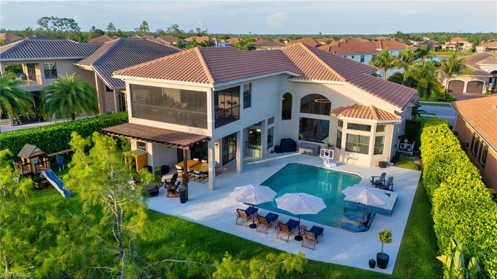 Expansive exterior featuring a large swimming pool with integrated spa, a screened-in second-story balcony, an outdoor covered patio with a pergola, a manicured lawn, and lush perimeter hedges