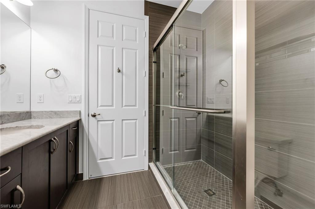 Modern bathroom featuring a frameless glass shower enclosure with horizontal gray tilework and diamond-patterned floor tiling