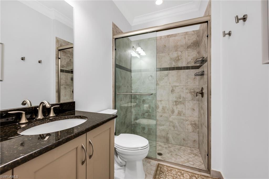 Glass-enclosed shower with tiled walls and flooring, complemented by a vanity featuring a dark stone countertop and undermount sink