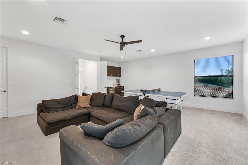 Spacious bonus/media room featuring recessed lighting, a ceiling fan, light-colored carpet, a built-in wet bar with dark wood cabinetry, and a large window