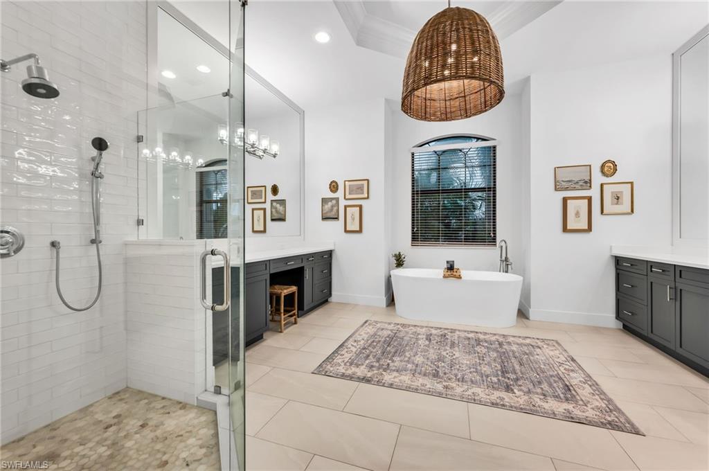 Spacious bathroom featuring a freestanding soaking tub, a large walk-in shower with glass enclosure, dual vanity cabinetry with light countertops, and neutral-toned floor tiling
