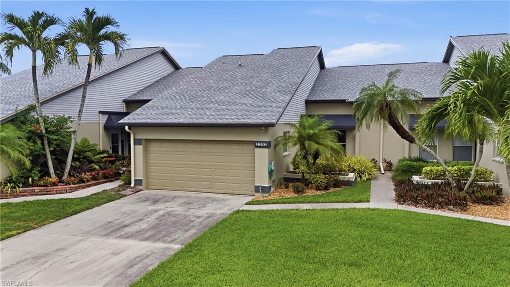 Exterior featuring a multi-gabled roof, neutral-toned siding and stucco, an integrated garage with a paneled door, a concrete driveway, and mature tropical landscaping