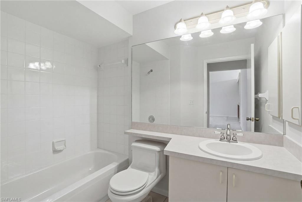 Full bathroom featuring a white bathtub with tiled surround, a toilet, and a vanity with an integrated sink and countertop