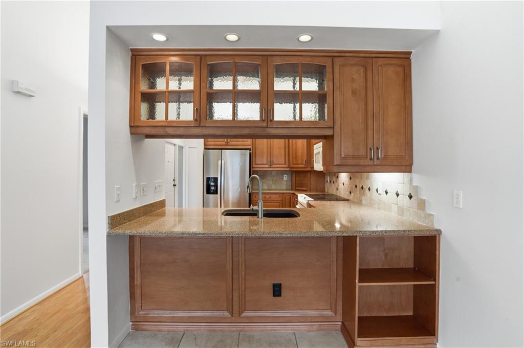 Kitchen pass-through featuring warm wood-finish cabinetry, illuminated glass-front upper cabinets, and recessed lighting