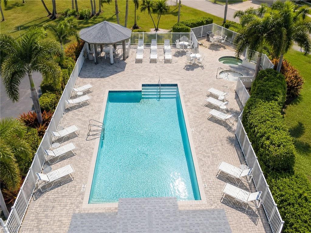 Paved pool deck featuring a rectangular swimming pool, two integrated spas, and a shaded gazebo