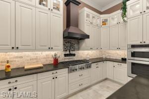 Gourmet kitchen featuring extensive white cabinetry, dark countertops, a professional-grade gas range with a matching range hood, and built-in double ovens